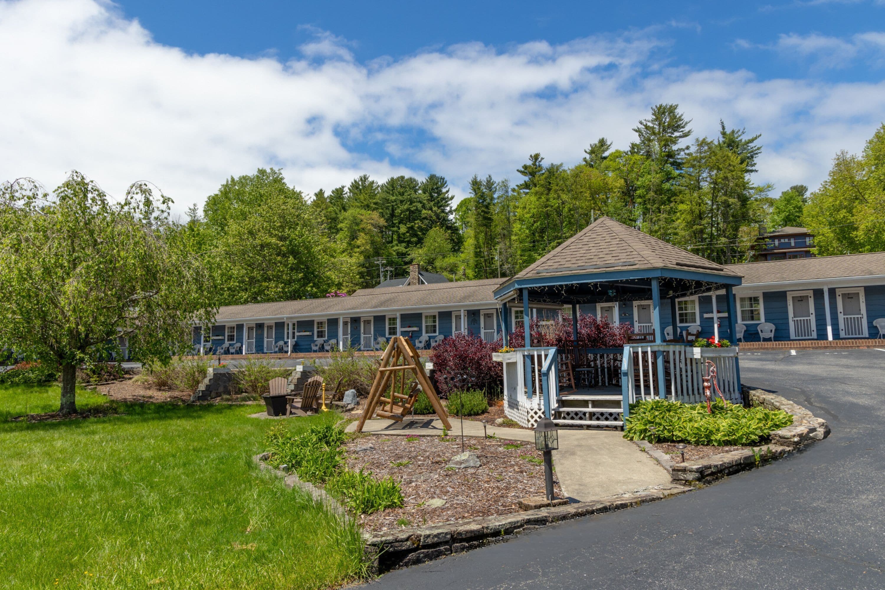 A motel with a blue exterior, a gazebo, and a swing set in the yard.
