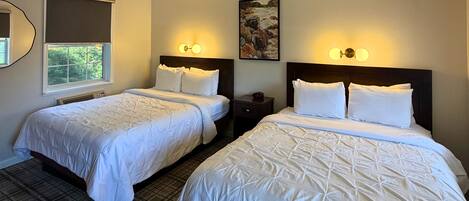 A hotel room with two beds, a window, a painting, and wall sconces.