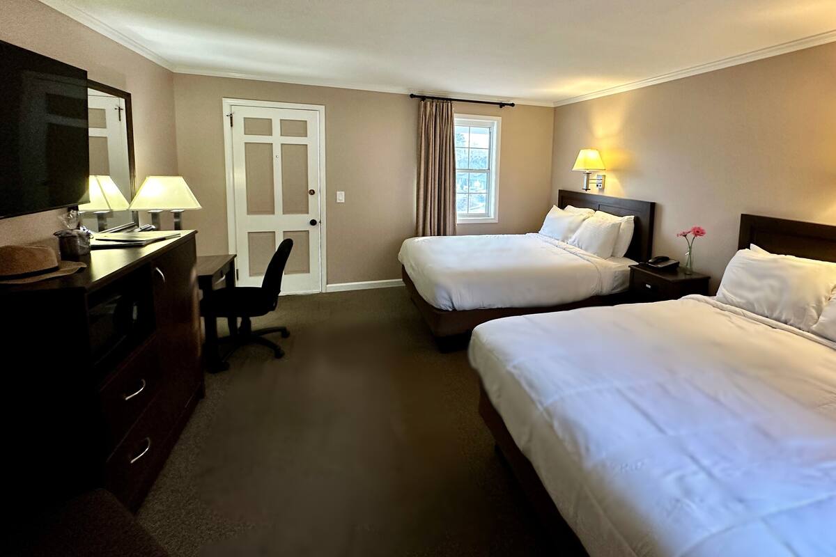 A hotel room with two beds, a desk, a chair, a TV, and a window with curtains.