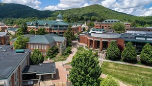 A campus with multiple buildings, including a prominent red brick building with a green roof, surrounded by green trees and a mountain in the background. - Blowing Rock Inn (Blowing Rock)