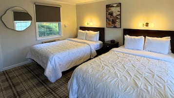 Une chambre d’hôtel avec deux lits, un grand miroir, un tableau et une fenêtre donnant sur des arbres.