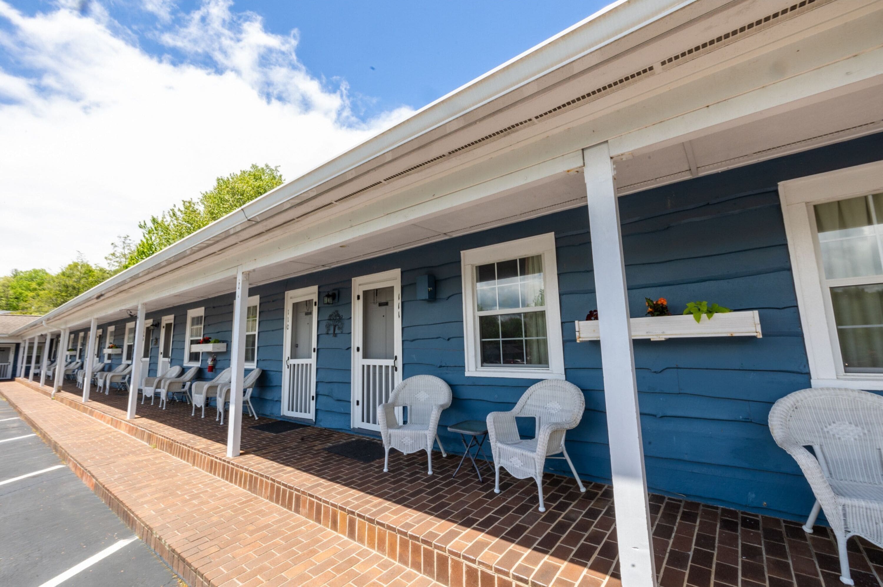 A motel with a row of rooms, each with a porch and white wicker chairs.