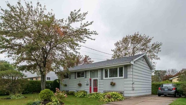 A single-story house with a red door, a small front yard, and a car parked in the driveway.