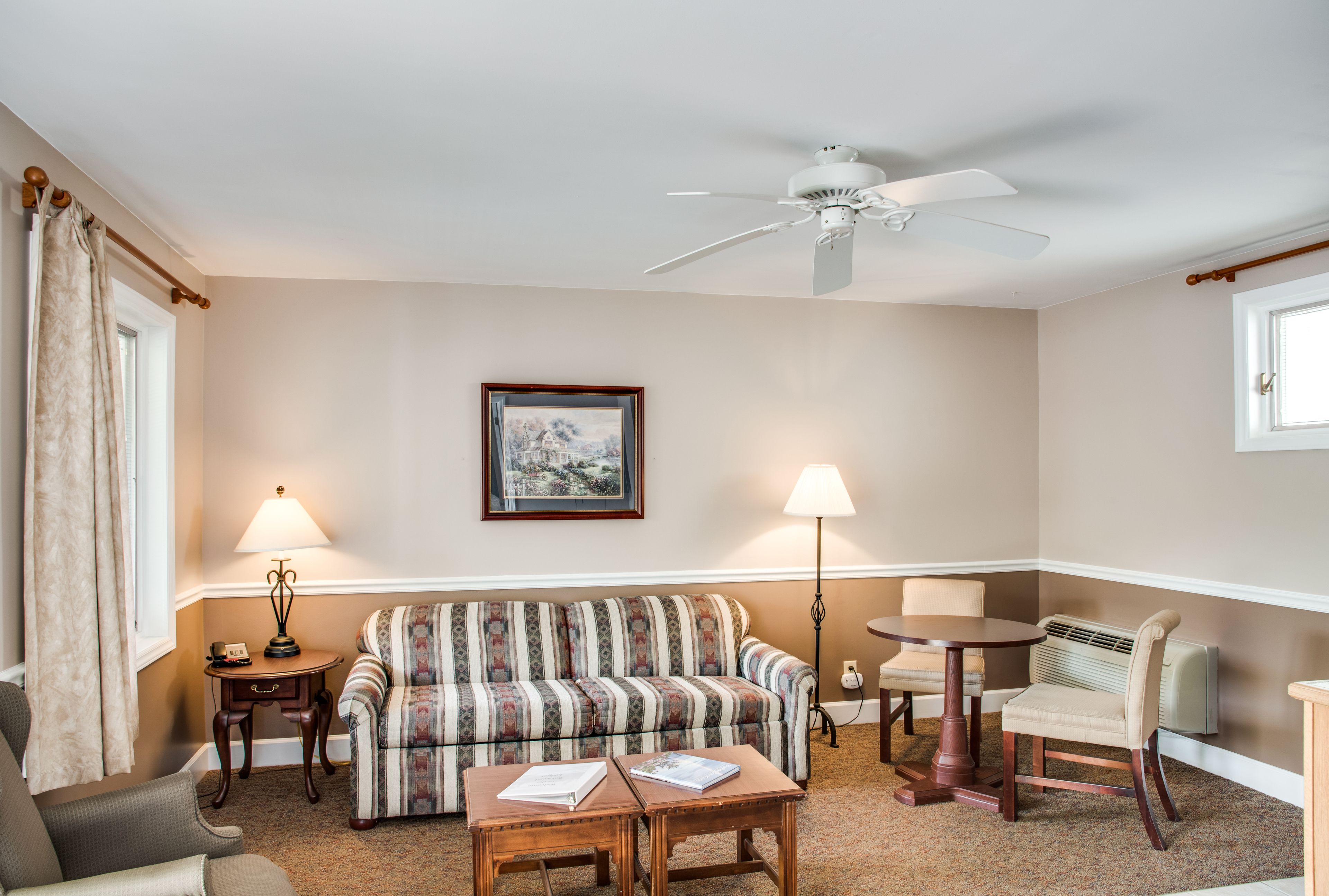 A living room with a sofa, two armchairs, a coffee table, a ceiling fan, and two lamps.
