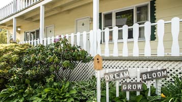 A house with a white picket fence, a wooden sign that says "DREAM BLOOM GROW", and lush green plants in front.