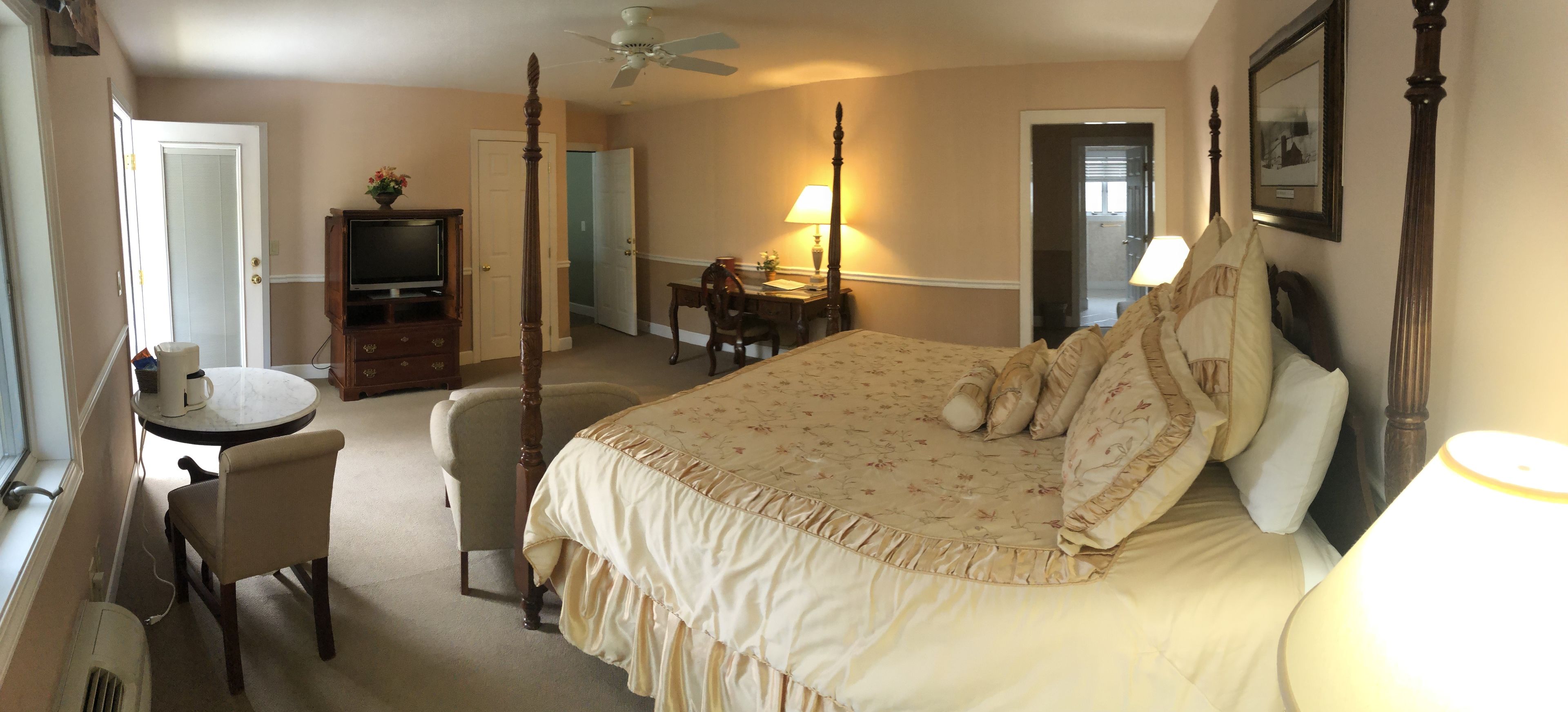 A bedroom with a four-poster bed, a desk with a chair, a television, and a lamp.