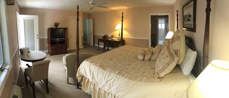 A bedroom with a four-poster bed, a desk with a chair, a television, and a lamp.