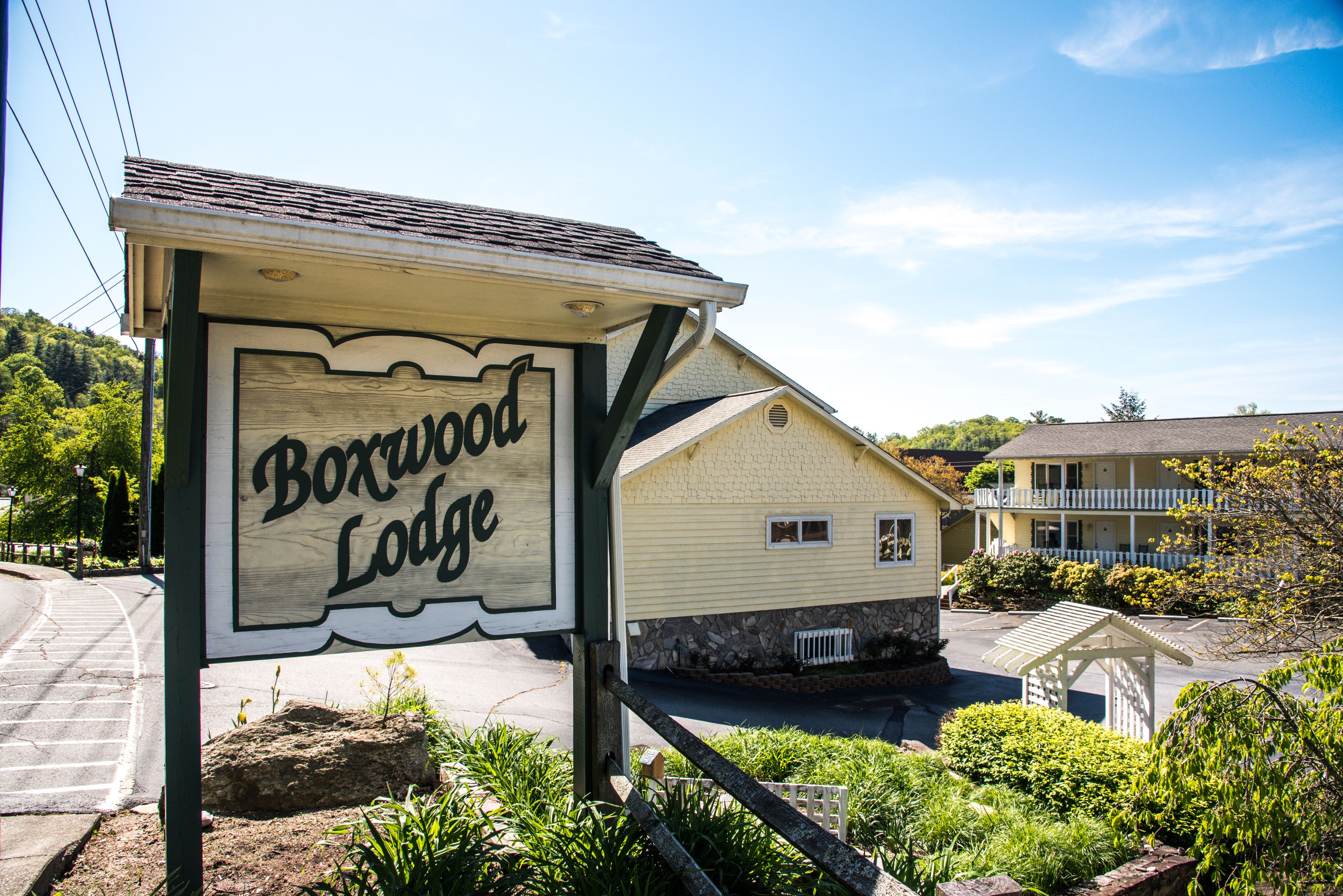 A wooden sign for Boxwood Lodge with a stone foundation and a small porch.