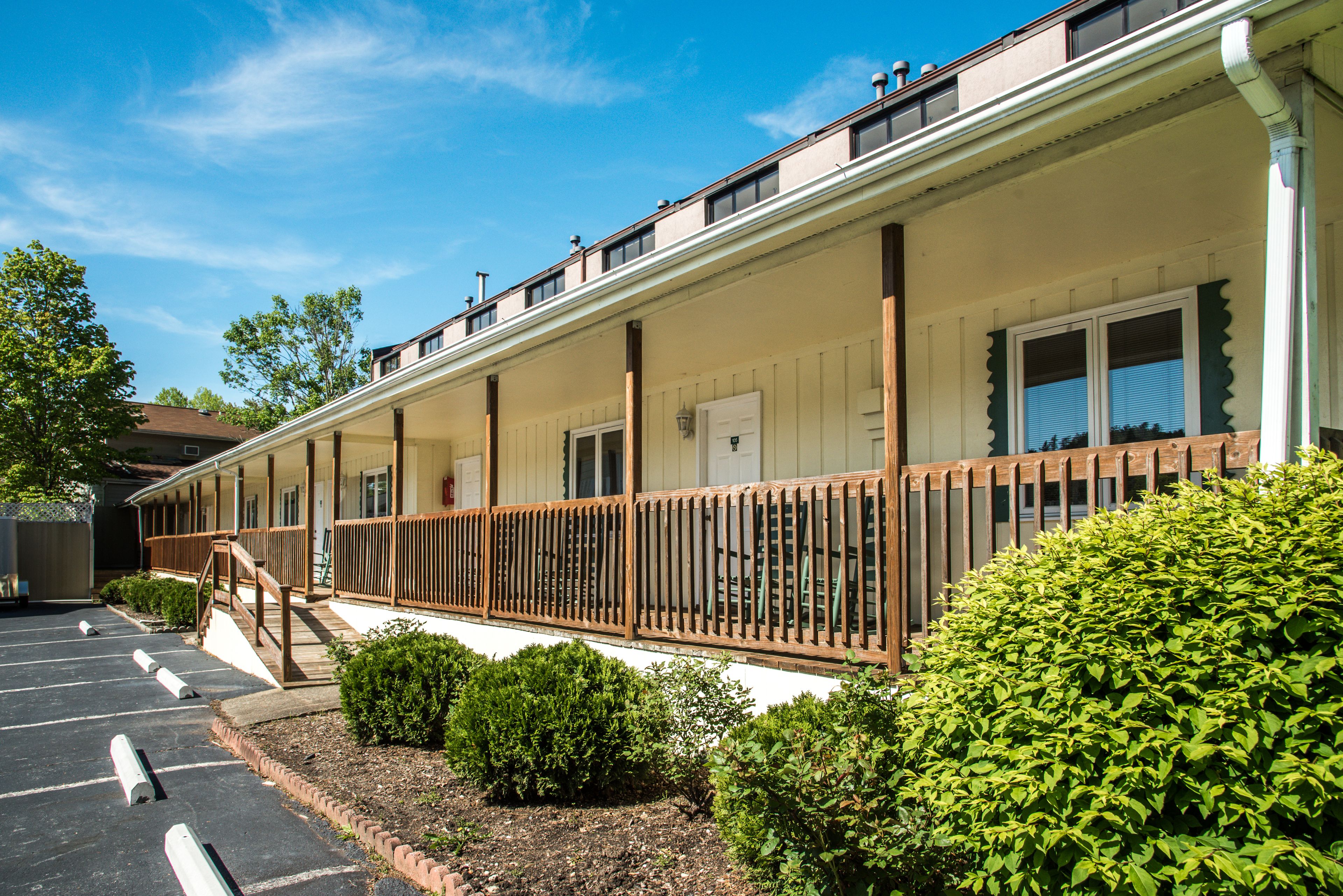 A motel with a covered porch, a parking lot, and well-maintained landscaping.