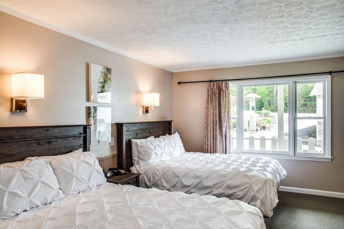 Une chambre d’hôtel avec deux lits, une table de chevet, des lampes fixées au mur, une fenêtre avec des rideaux et une vue sur l’extérieur.