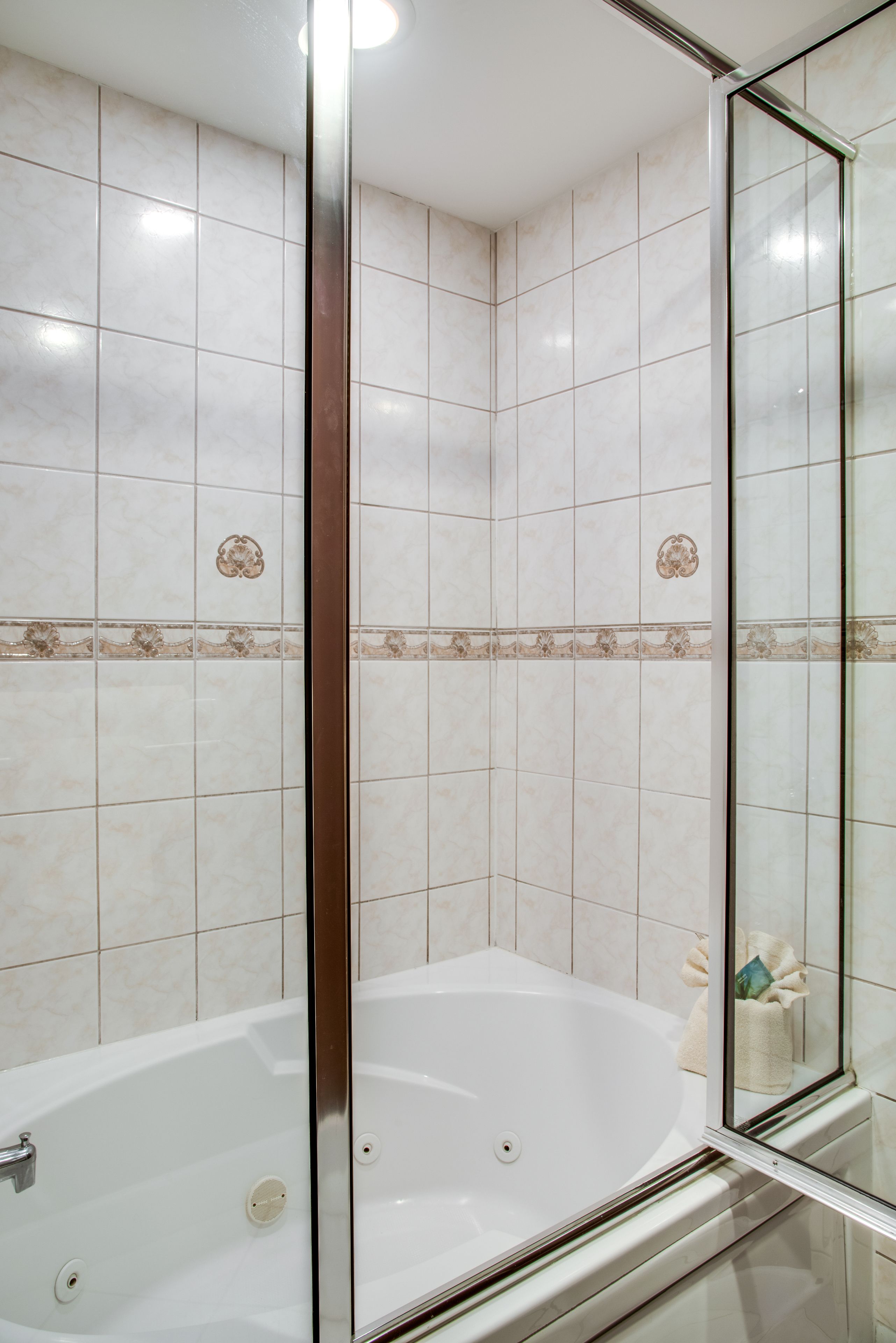 A modern bathroom with a glass-enclosed shower, a white bathtub, and decorative tiles.