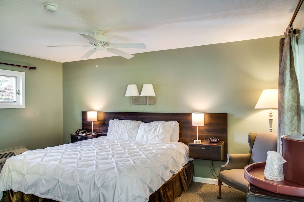 Une chambre d’hôtel comprenant un lit, deux tables de chevet avec des lampes, une chaise et un ventilateur de plafond.