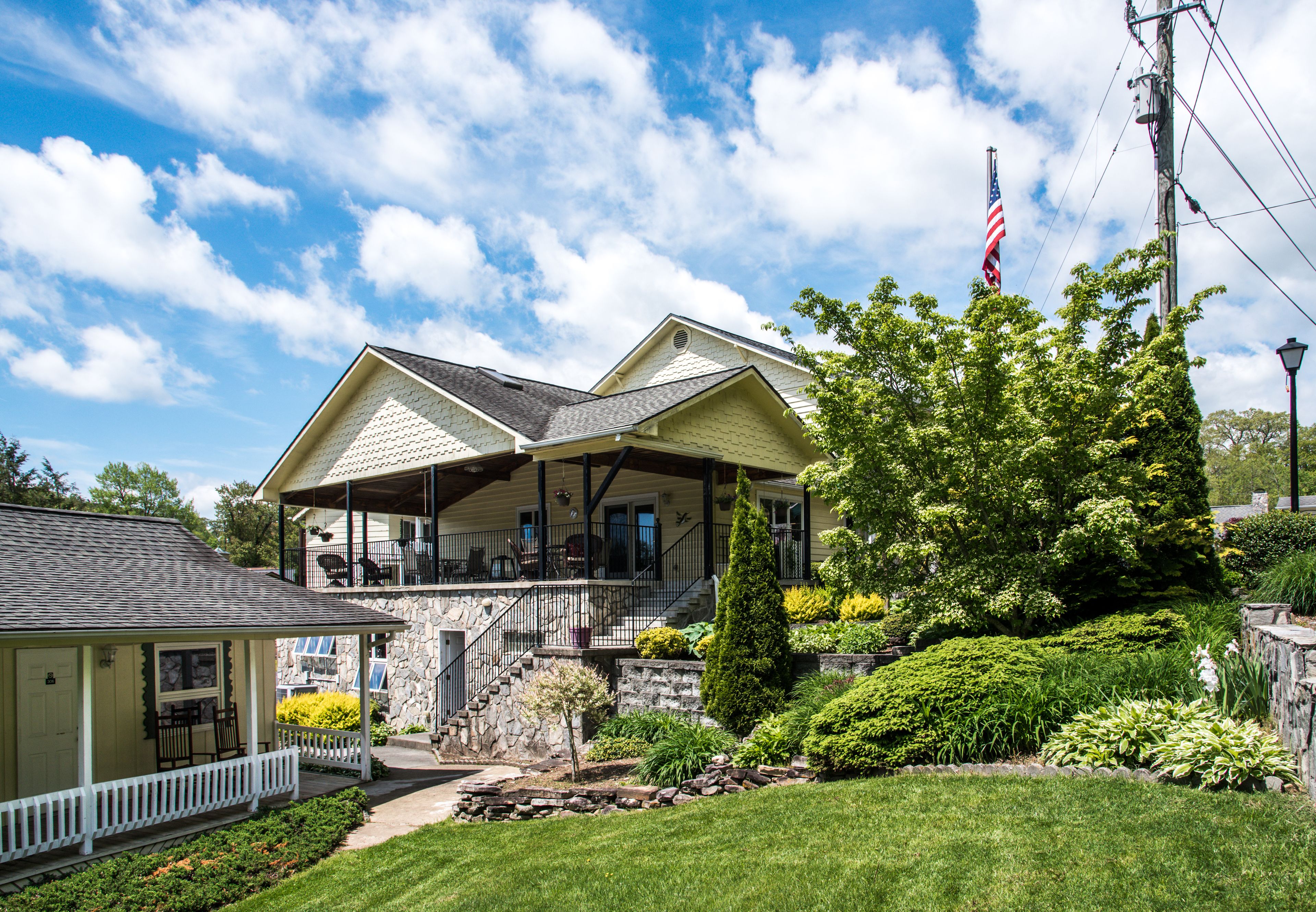 A two-story house with a porch, stone steps, and a flagpole.