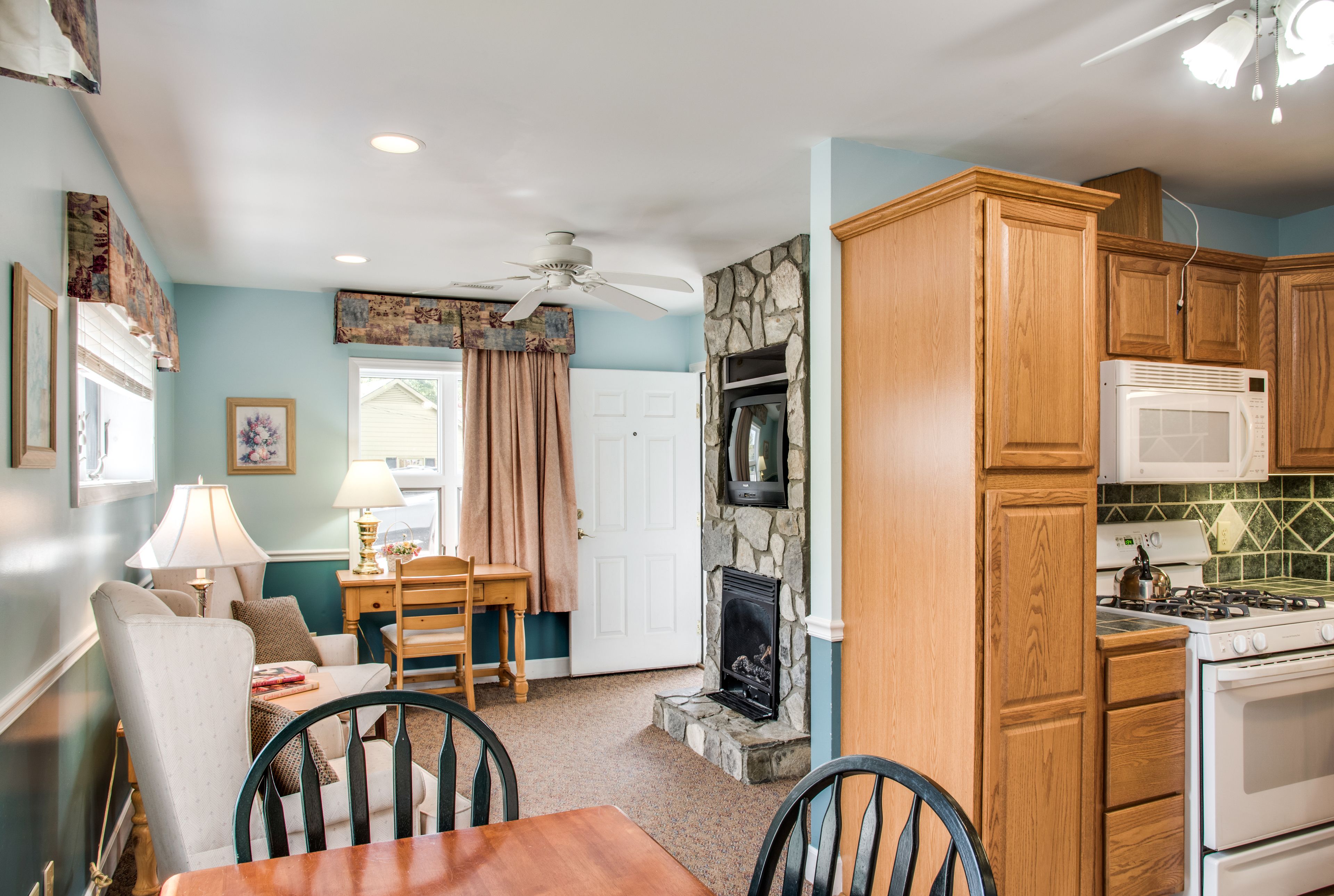A kitchen with wooden cabinets, a stone fireplace, a microwave, and a stove.