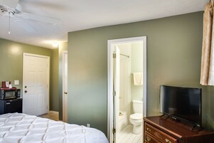 Habitación de hotel con cama, un televisor sobre una cómoda de madera, microondas y puerta que da a un baño.