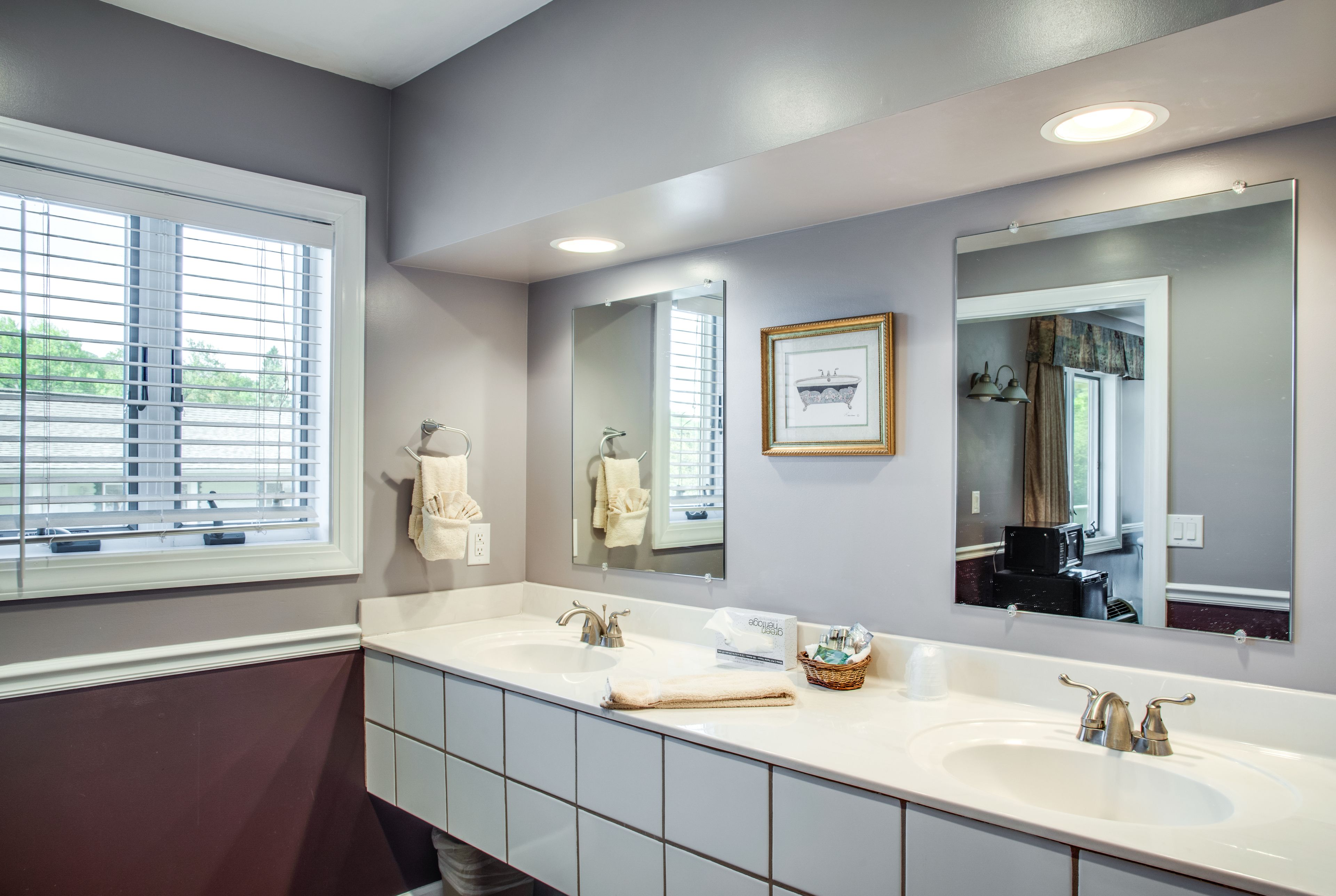 A bathroom with a double sink, large mirrors, and a window with blinds.