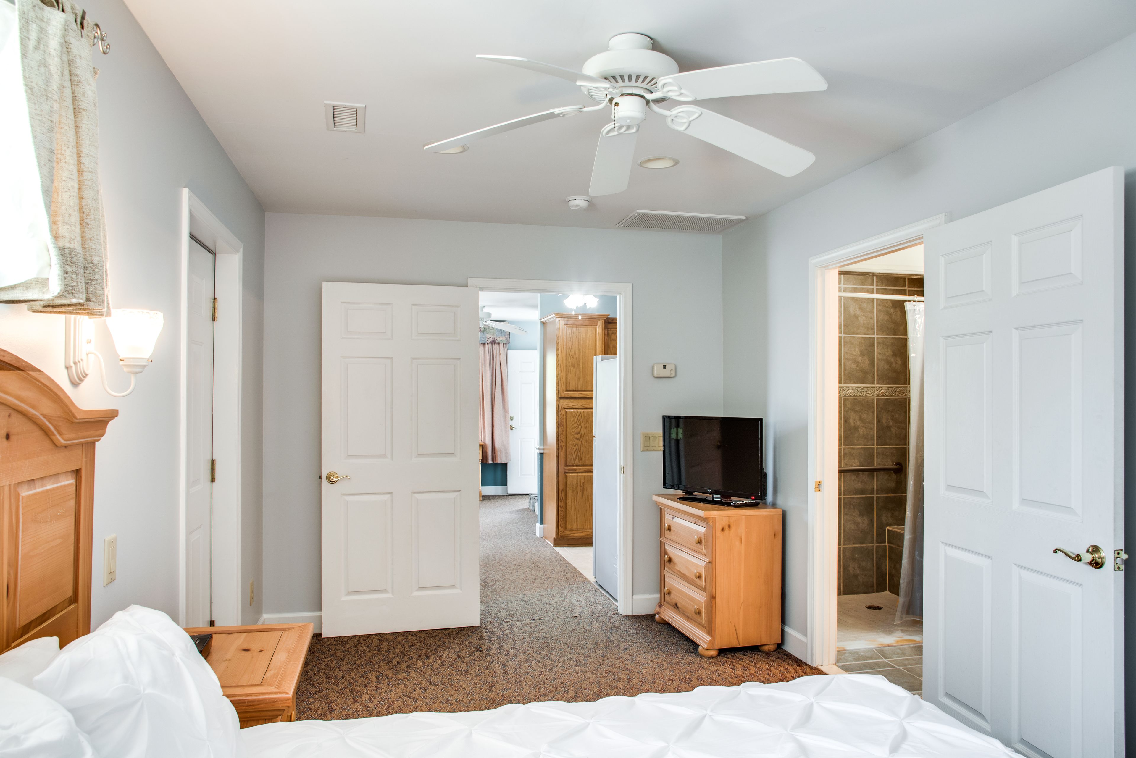 Een slaapkamer met een bed, een plafondventilator, een televisie op een houten dressoir en een inloopkast.