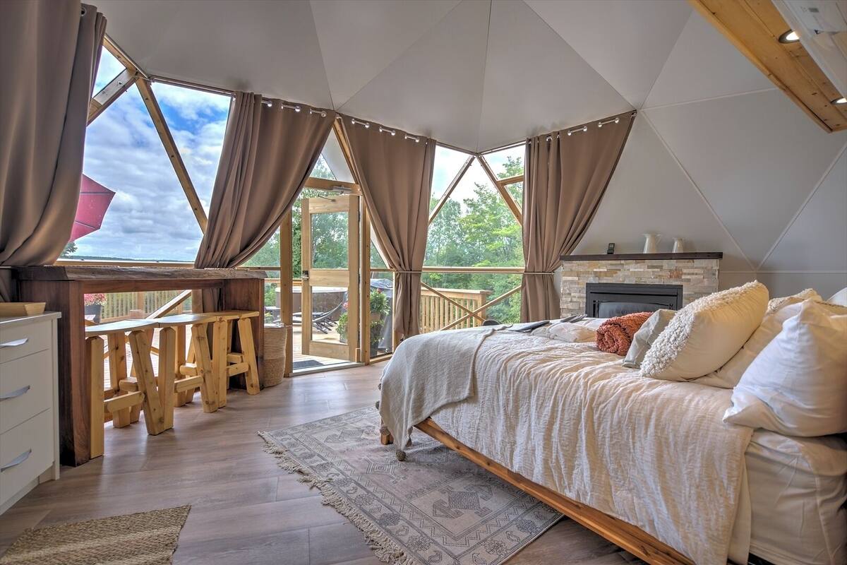 Ein Schlafzimmer mit einem großen Bett, einem Holztisch und Blick ins Freie durch ein großes Fenster.