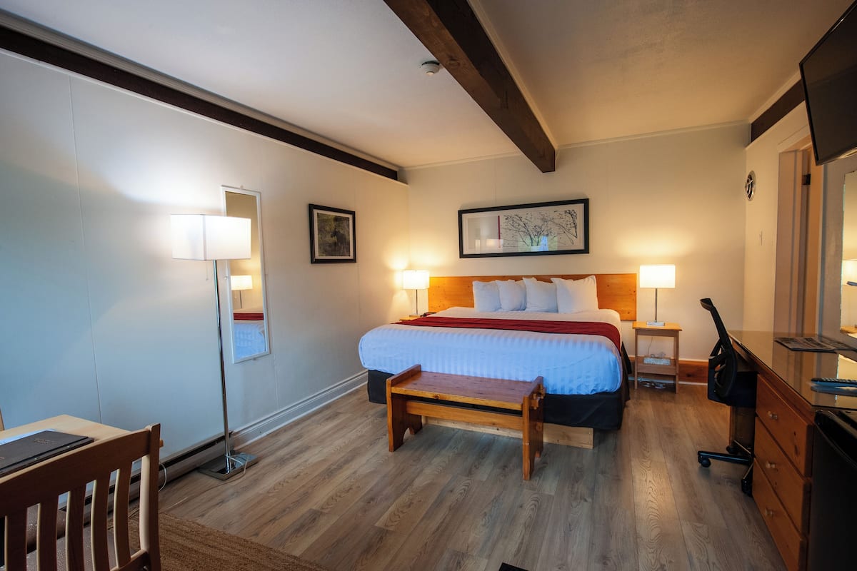 Ein Hotelzimmer mit Bett, Nachttischlampen, Schreibtisch, Stuhl und einer Holzbank.