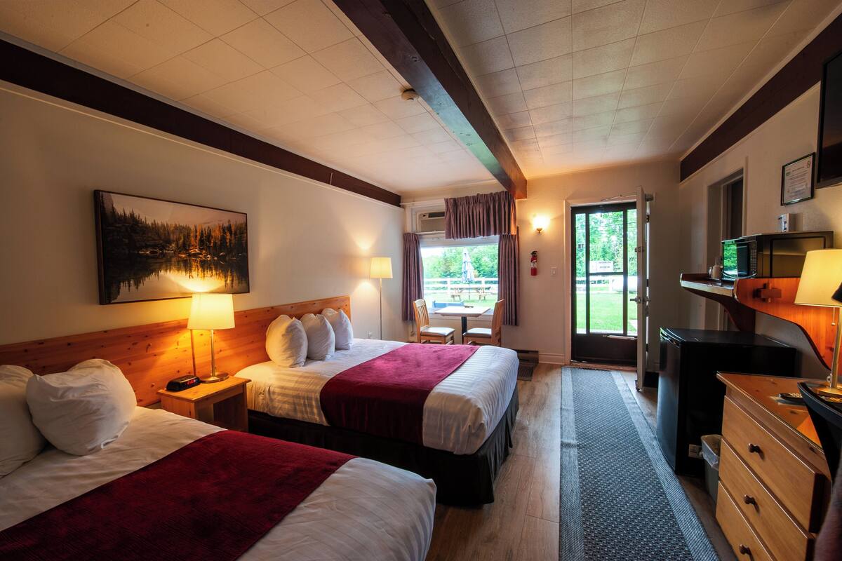 Ein Hotelzimmer mit zwei Betten, einem Schreibtisch mit Computer, einer Lampe und einem Bild an der Wand.