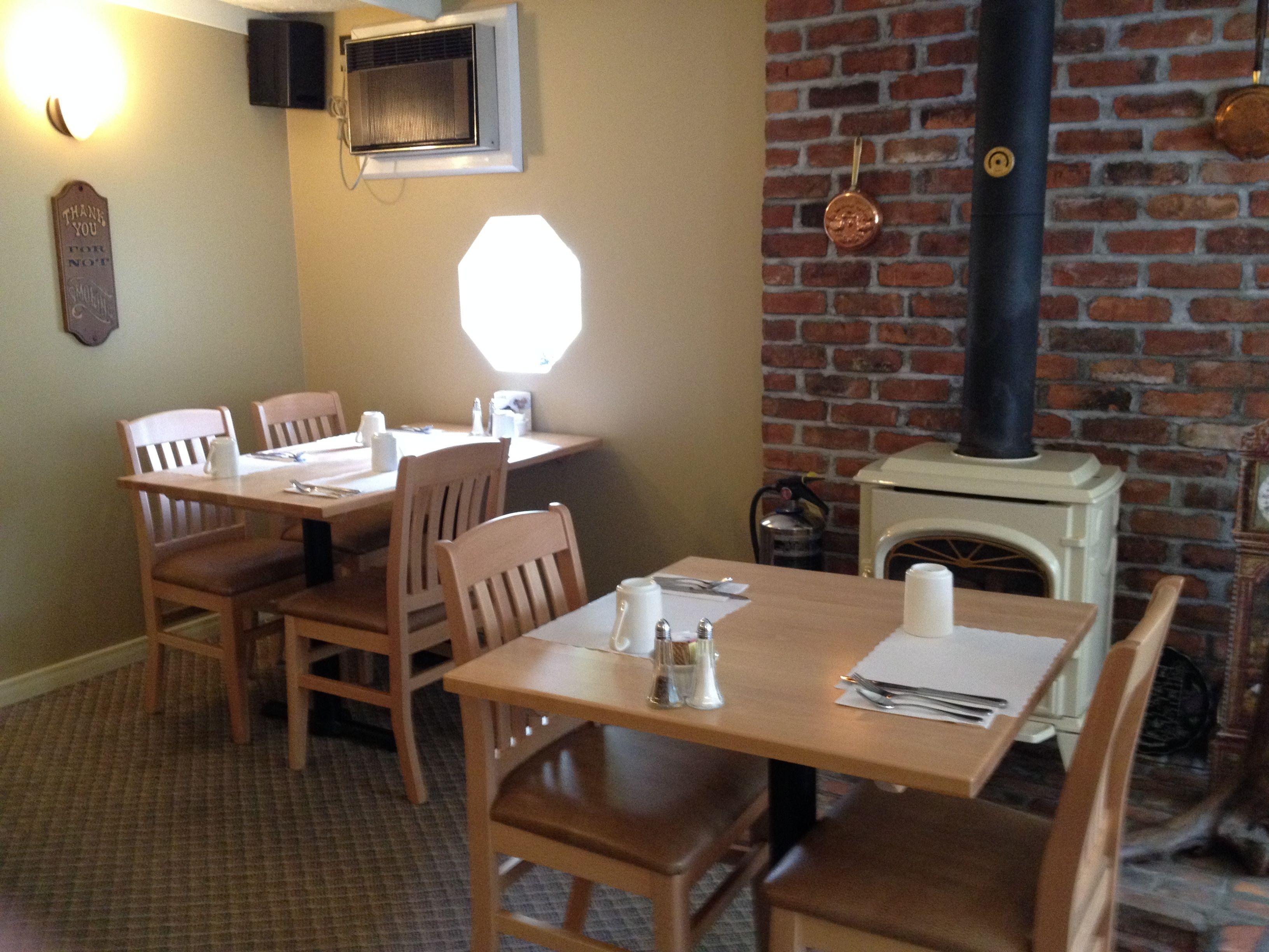 A dining area with wooden tables and chairs, a brick wall, and a fireplace with a chimney.