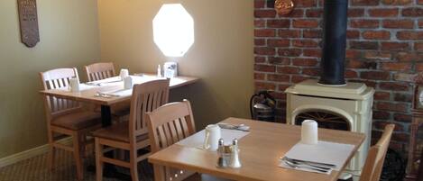 A dining area with wooden tables and chairs, a brick wall, and a fireplace with a chimney.