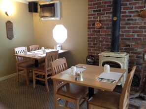 A dining area with wooden tables and chairs, a brick wall, and a fireplace with a chimney.
