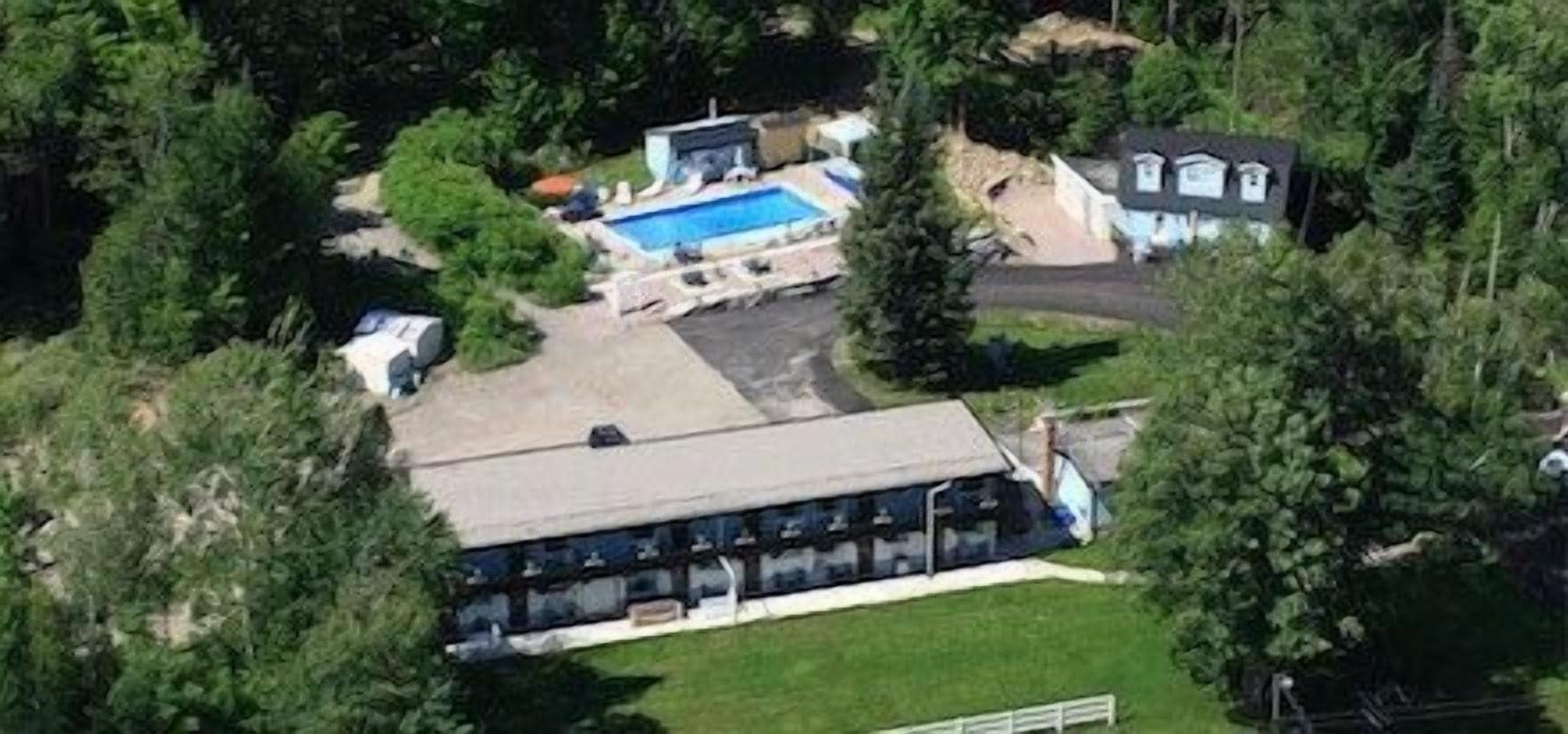 An aerial view of a motel with a swimming pool, a covered parking area, and a large building with a flat roof.