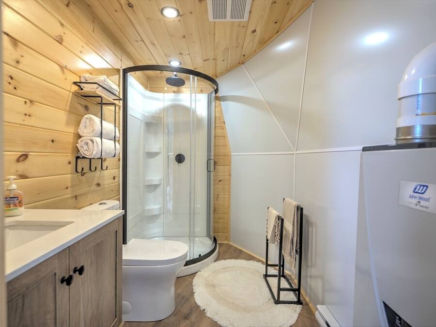 A modern bathroom with a glass shower enclosure, a white toilet, a sink with a soap dispenser, and a towel rack.
