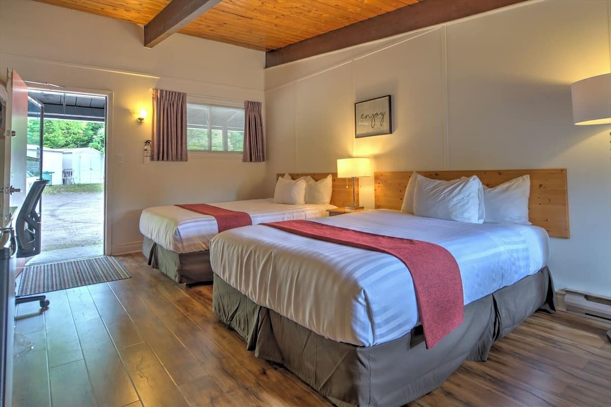 Ein Hotelzimmer mit zwei Betten, Holzboden, einer Bank und Blick ins Freie.