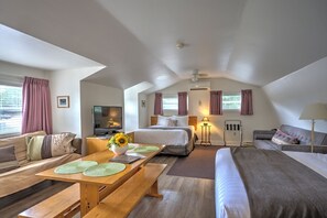 A hotel room with a bed, a sofa, a dining table, a TV, and a ceiling fan.