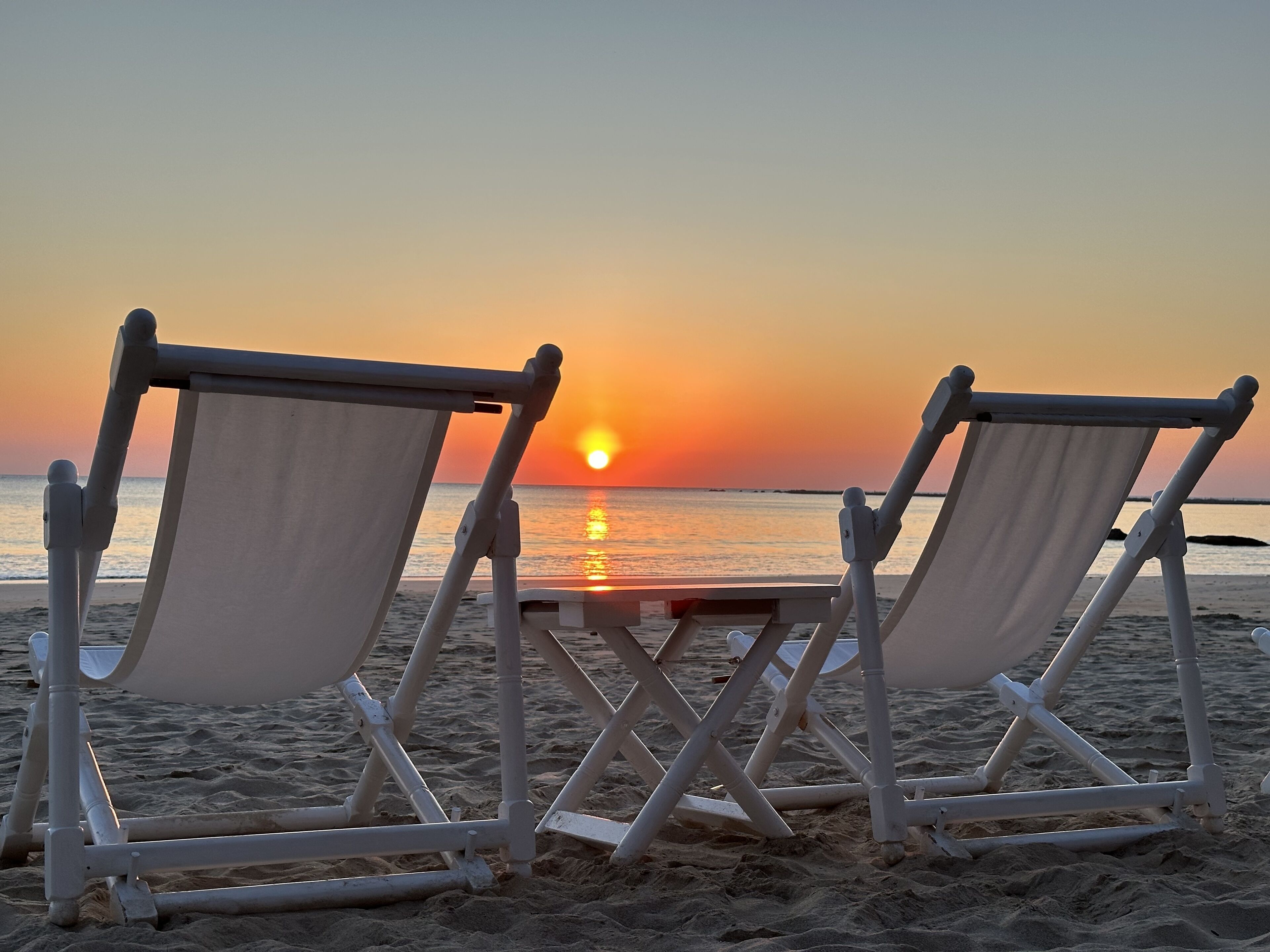 Two beach chairs facing the ocean at sunset.