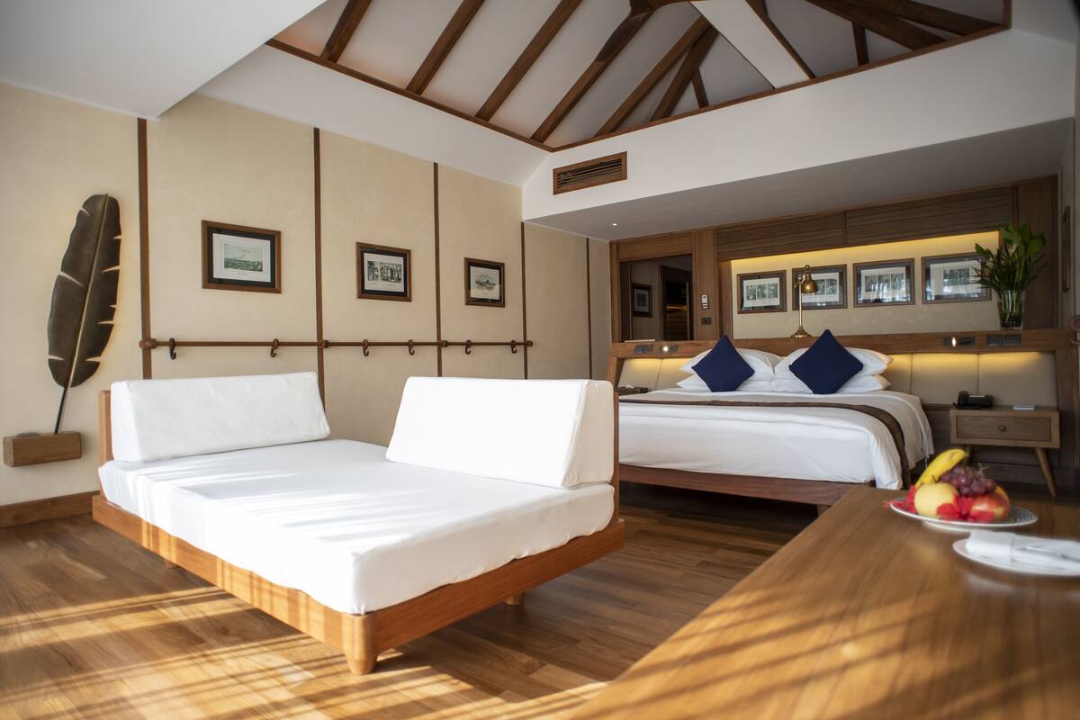 A hotel room with two beds, wooden flooring, and framed pictures on the walls.