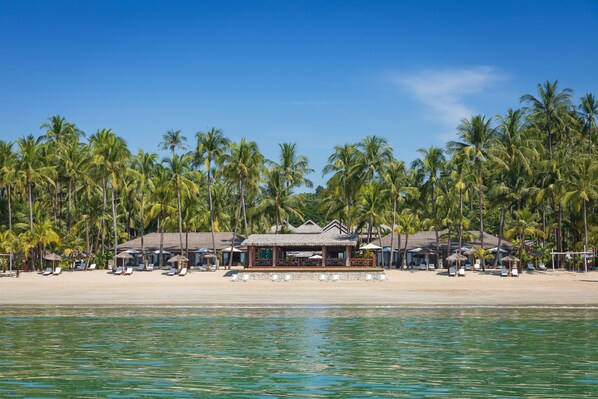 A beachfront hotel with multiple thatched-roof structures, sun loungers, and palm trees. - Bayview The Beach Resort (Ngapali)