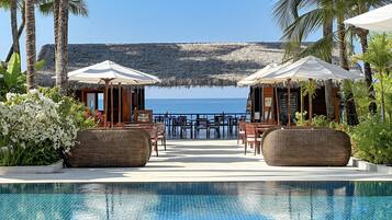 A poolside area with lounge chairs and umbrellas, overlooking a beach with a rocky outcrop in the distance.