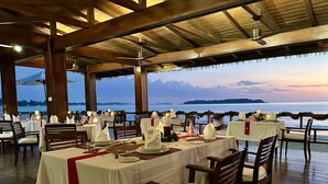 An outdoor dining area with tables set for a meal, overlooking a body of water. - Bayview The Beach Resort (Ngapali)