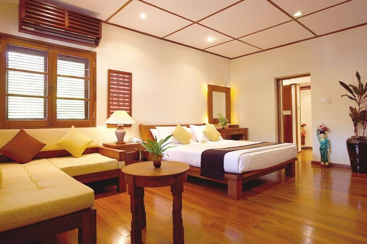 A hotel room with a bed, a sofa, a small table, and a potted plant.