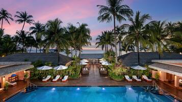 Relax by the ocean-view pool surrounded by lounge chairs and umbrellas under the shade of palm trees.
