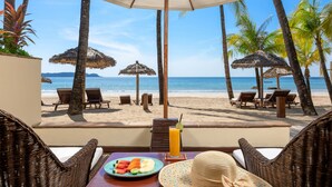 A beach view from a balcony with wicker furniture, a table with a plate of fruit, a drink, and a straw hat. - Bayview The Beach Resort (Ngapali)