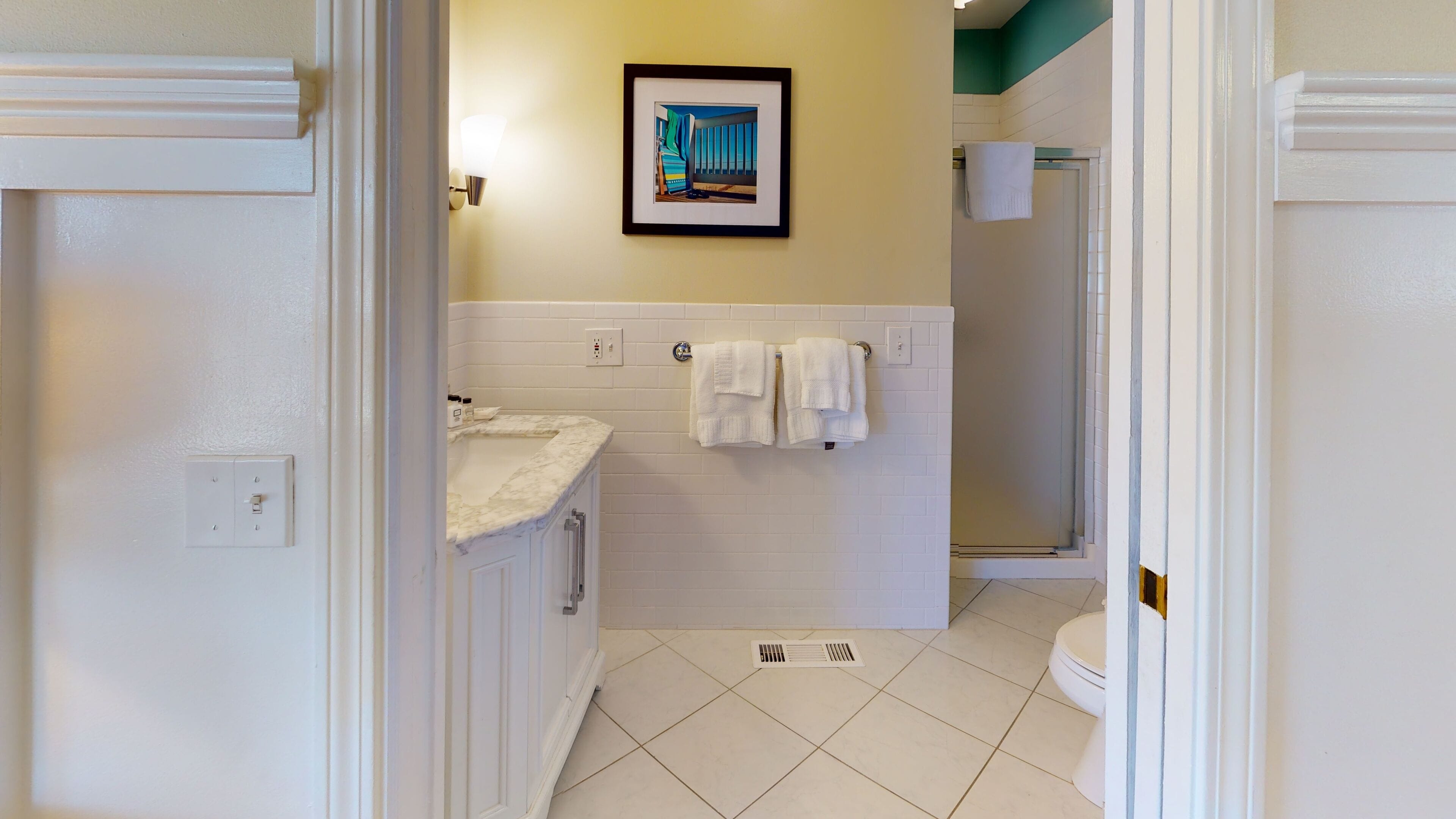 A bathroom with a white sink, a framed picture on the wall, and two white towels hanging on a rack.