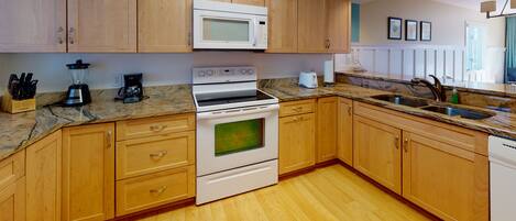 A kitchen with wooden cabinets, a white microwave, a stove, a sink, and a granite countertop.