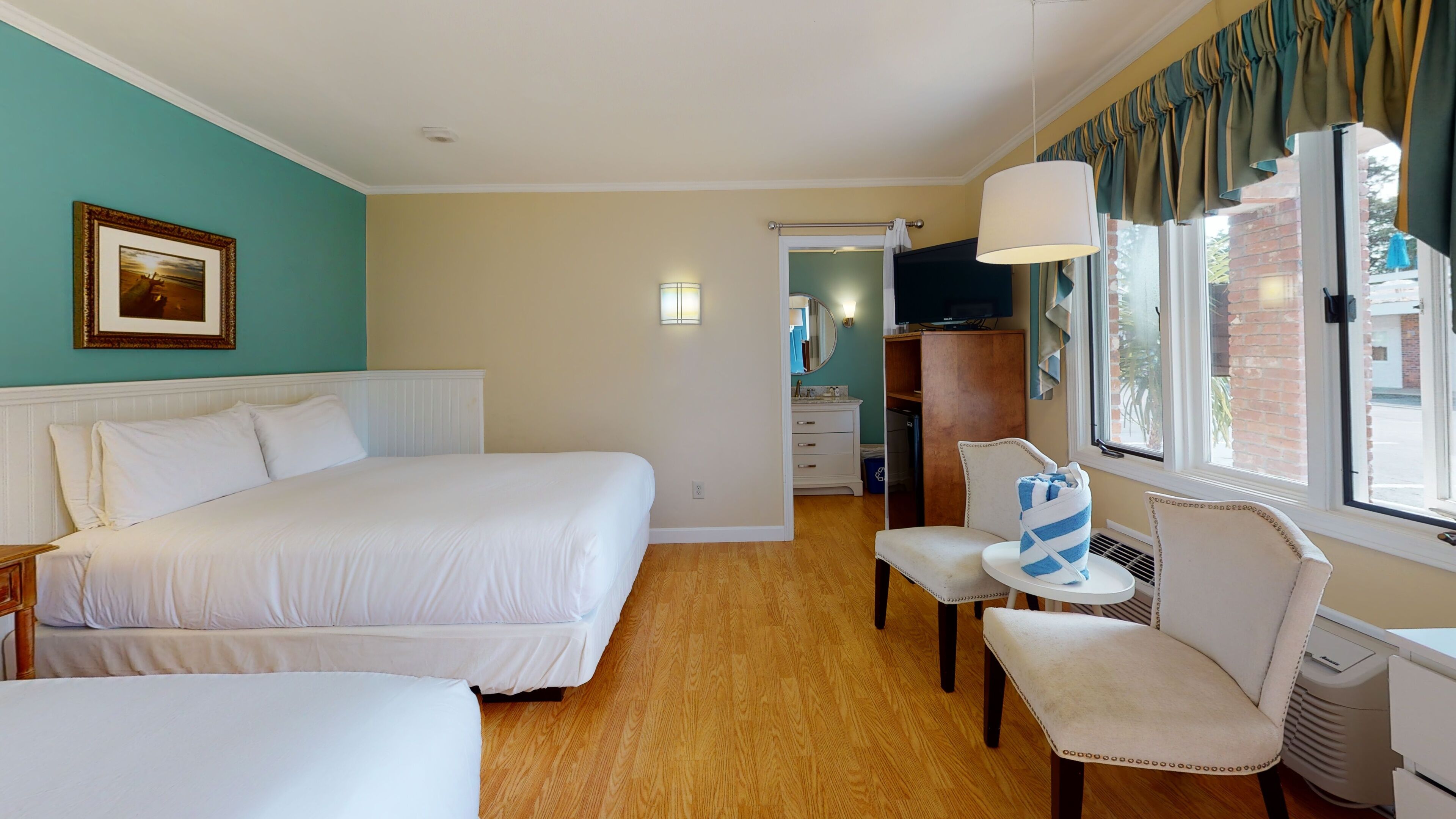 Ein Hotelzimmer mit einem großen Bett, einem Sessel, einem kleinen Tisch, einem Fernseher und einem Fenster mit Vorhängen.