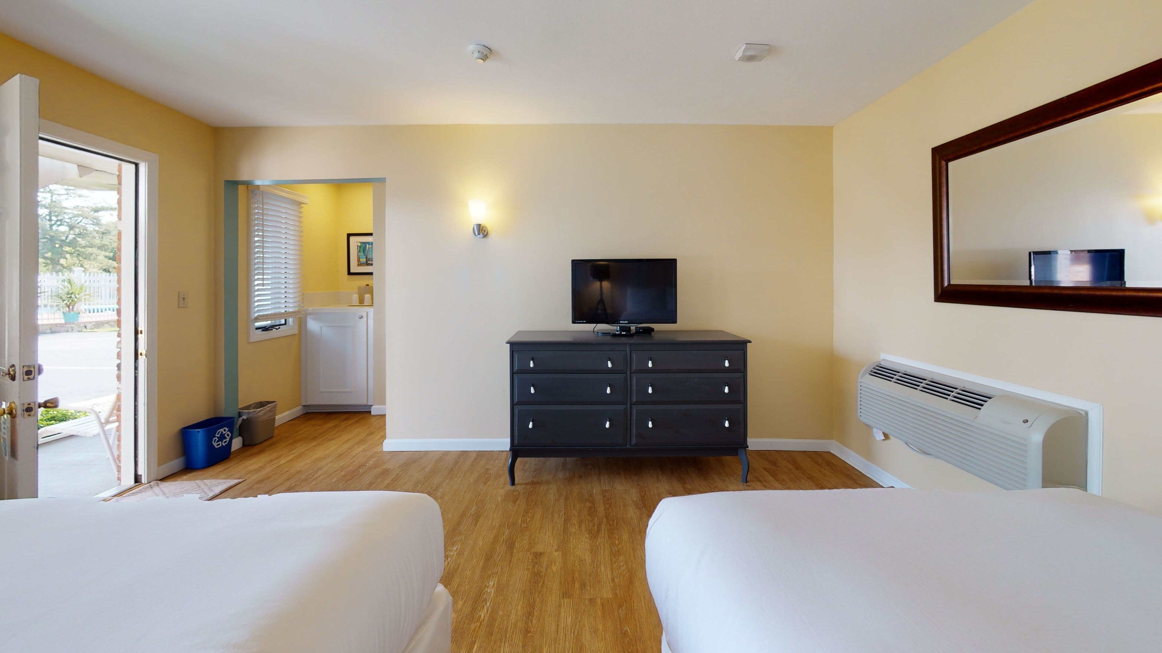 A hotel room with two beds, a dresser, a television, and a radiator.