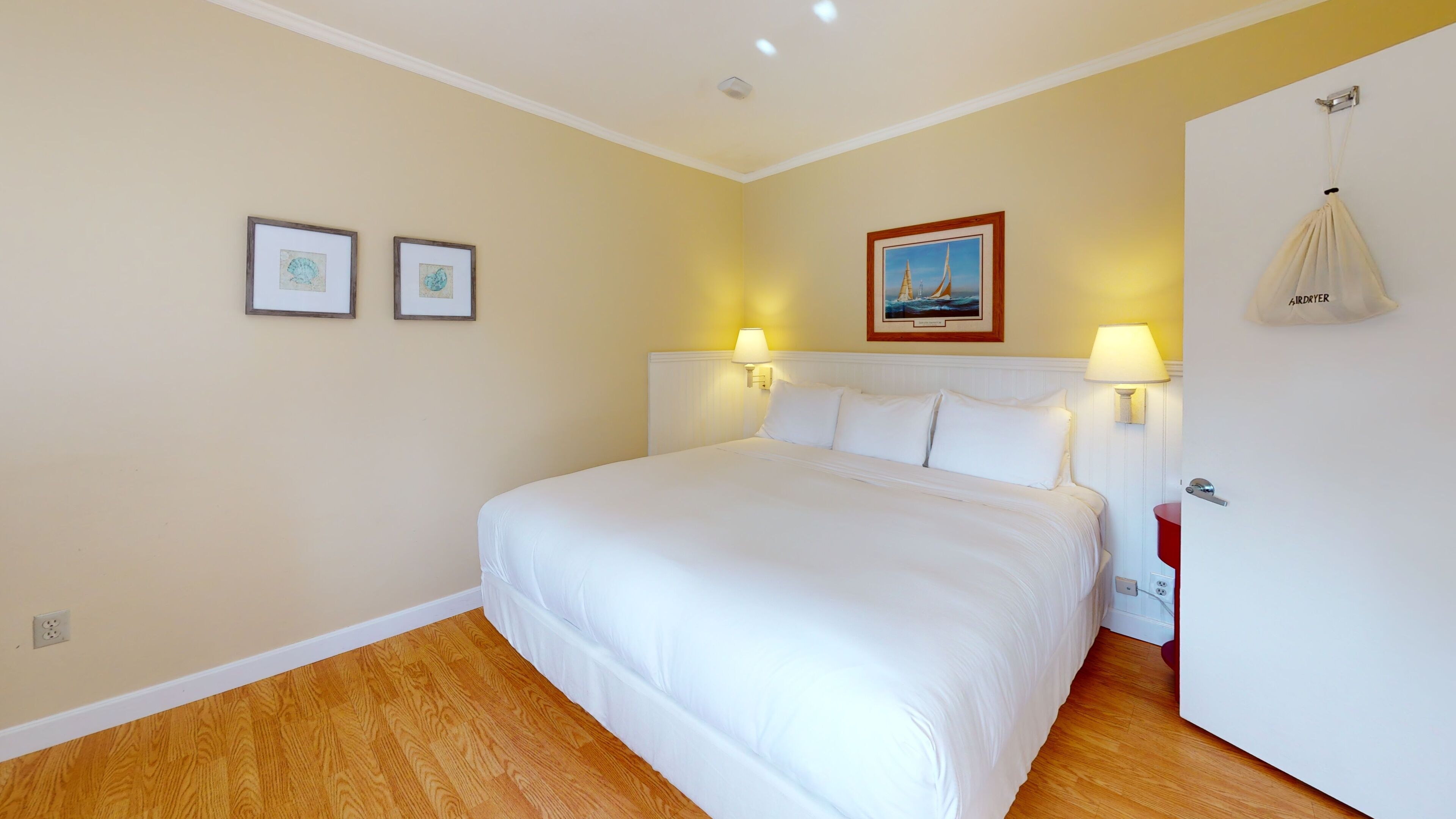 Une chambre d’hôtel avec un grand lit, deux lampes fixées au mur et une porte sur laquelle est accroché un sac.