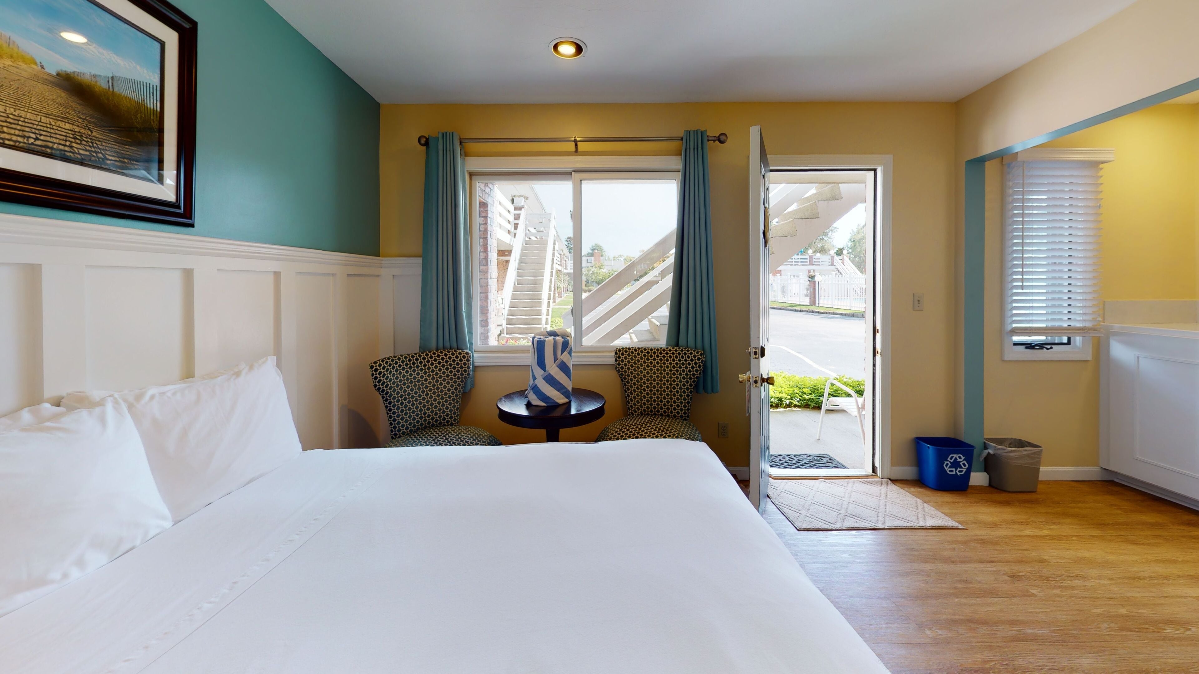 Une chambre d’hôtel avec un grand lit, deux fauteuils à motifs, une petite table et une vue sur l’extérieur.
