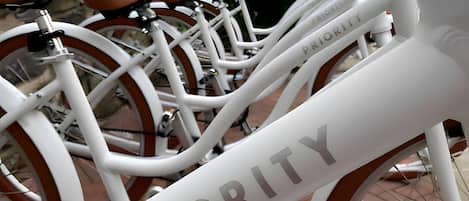 A white bicycle with the word "PRIORITY" on the frame, parked on a brick pavement.
