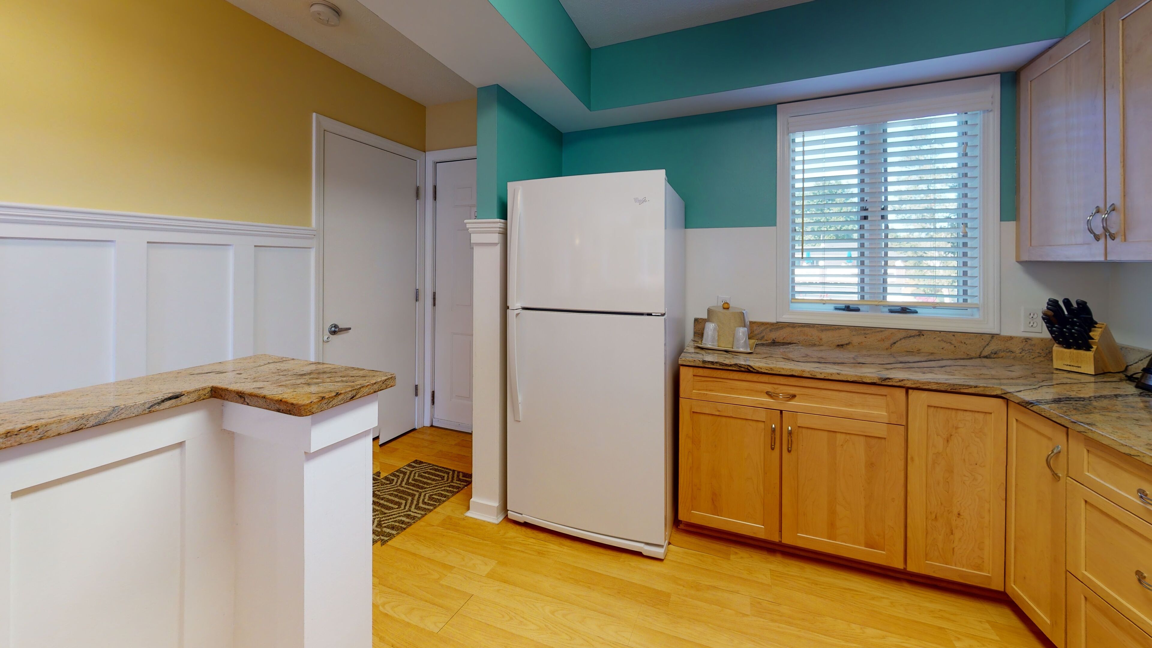 Una cocina con armarios blancos, un refrigerador blanco, una encimera de madera y una ventana con persianas.