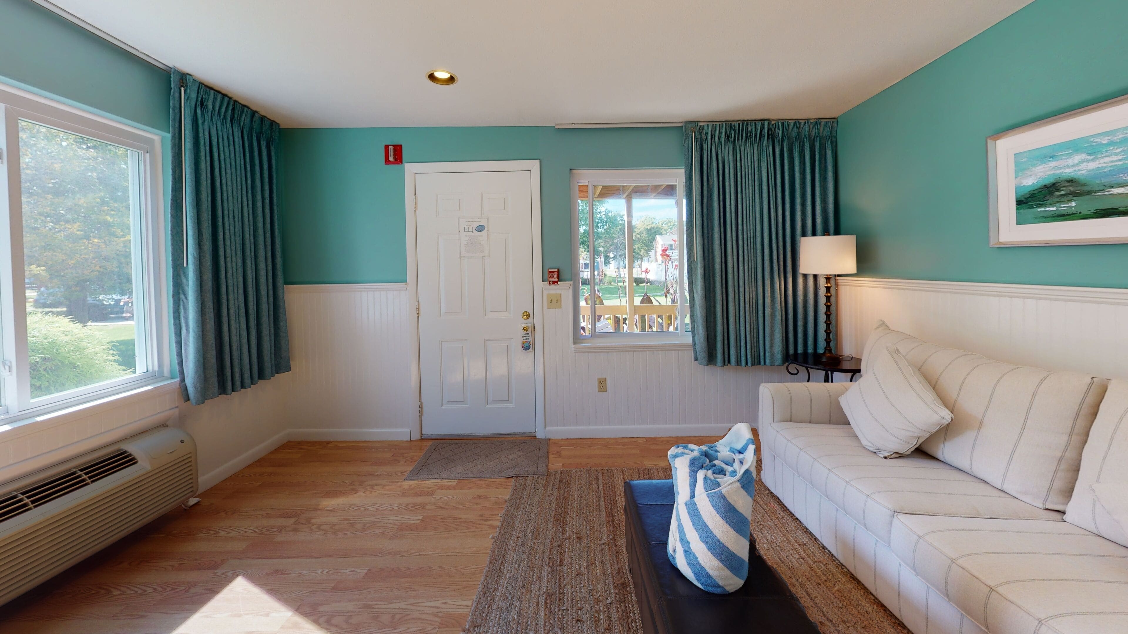 A room with a white couch, teal walls, a door with a window, and a view of the outdoors.