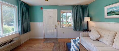 A room with a white couch, teal walls, a door with a window, and a view of the outdoors.