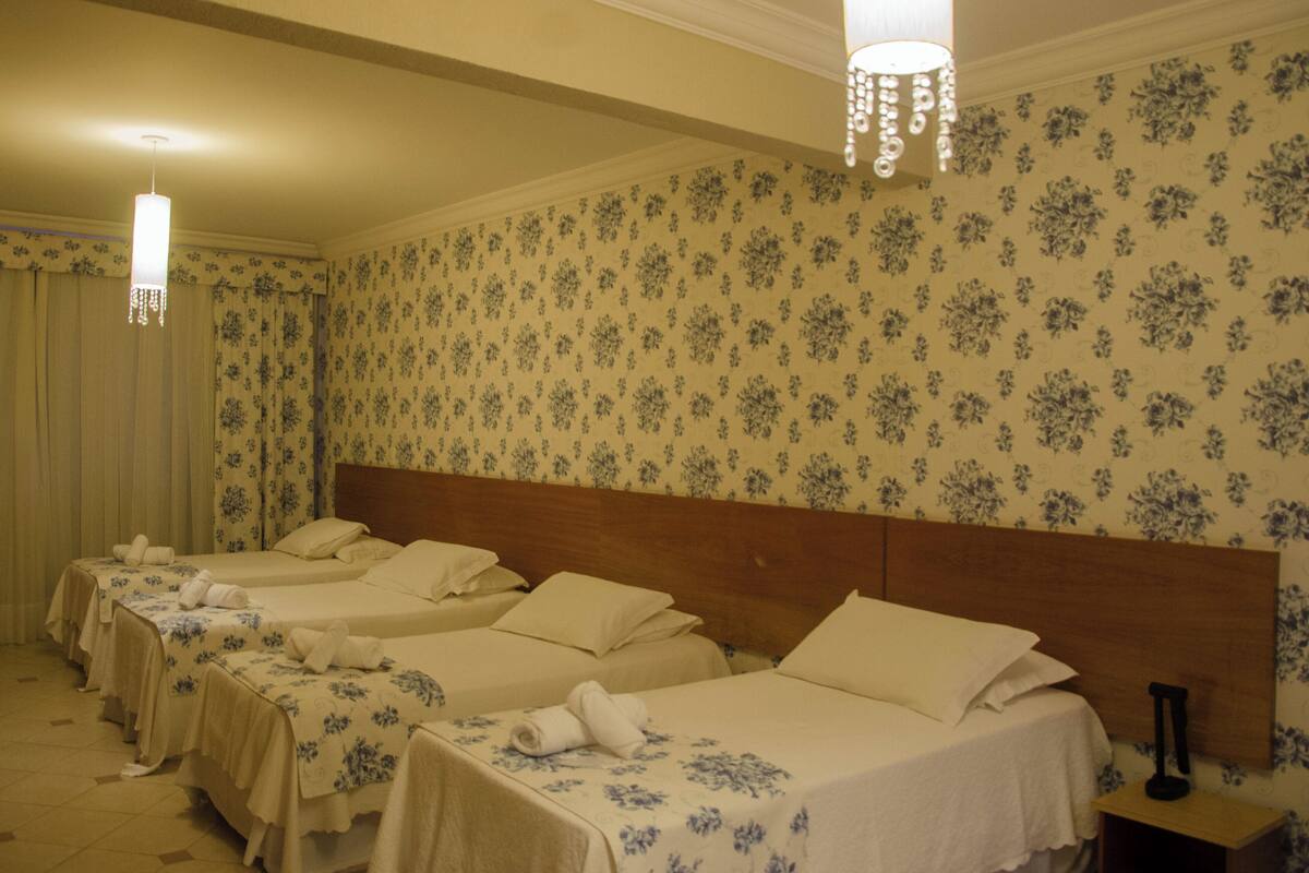 Habitación de hotel con cuatro camas individuales, papel tapiz floral y un candelabro.